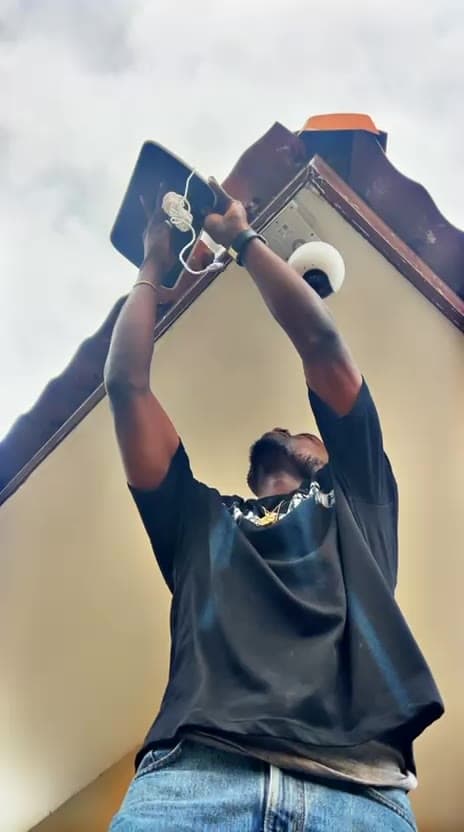 Technician mounting an external security camera and floodlight under a roof eave