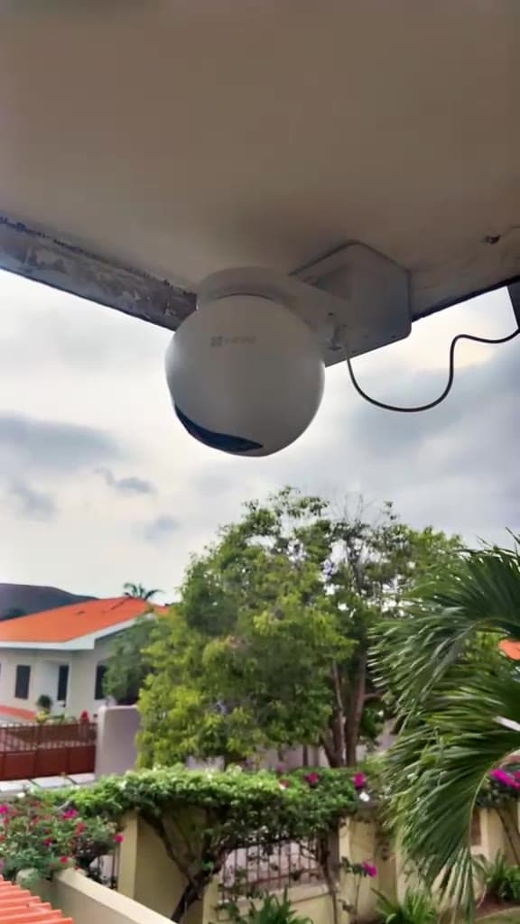 External dome camera mounted under a roof eave overlooking a walled compound