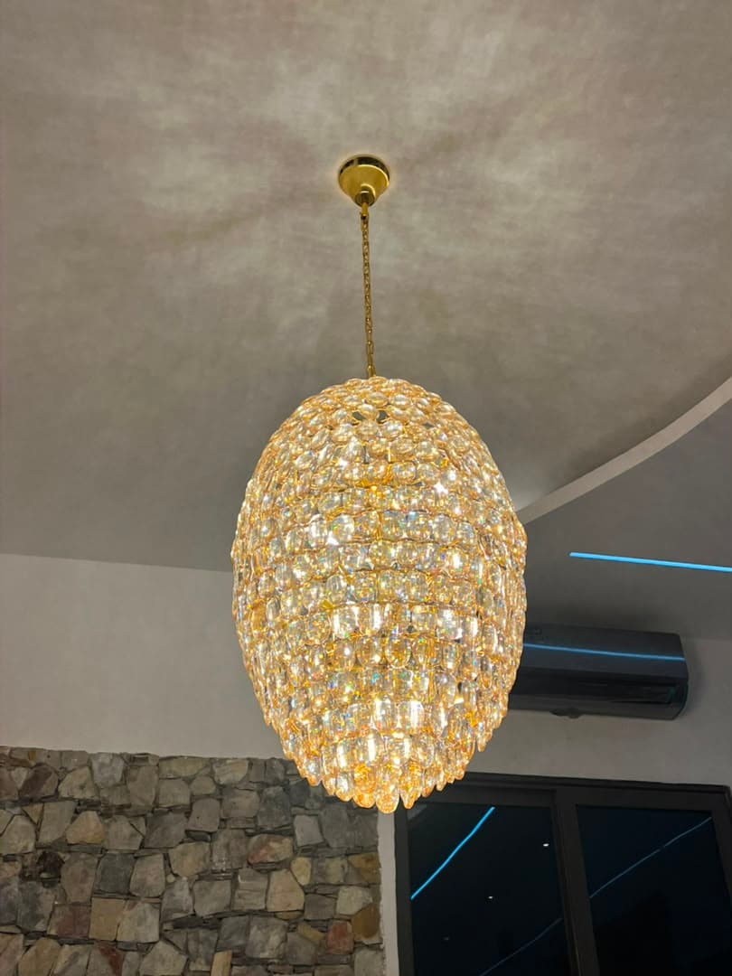 Installed crystal chandelier hanging from a high ceiling above a stone feature wall