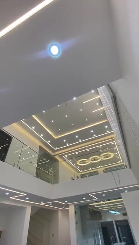 Double-height interior lit by recessed linear LED profiles, cove lighting and downlights set into a shaped ceiling