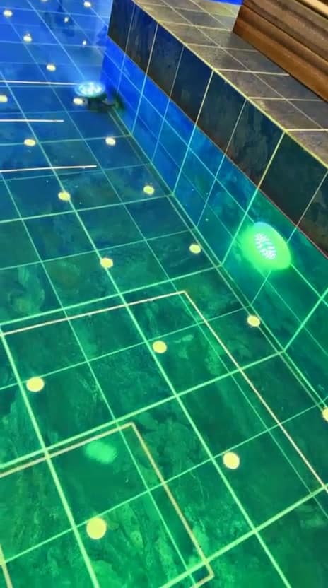Underwater colour-changing LED lights illuminating a tiled swimming pool in green and blue